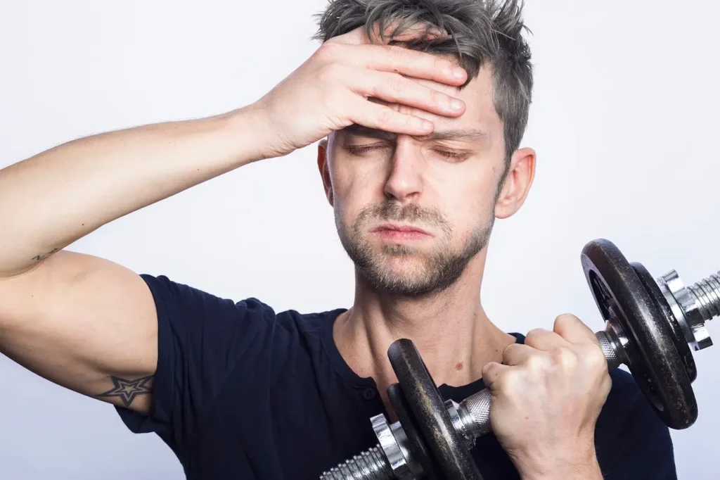 A man holding a dumbbell in one hand and looking troubled.