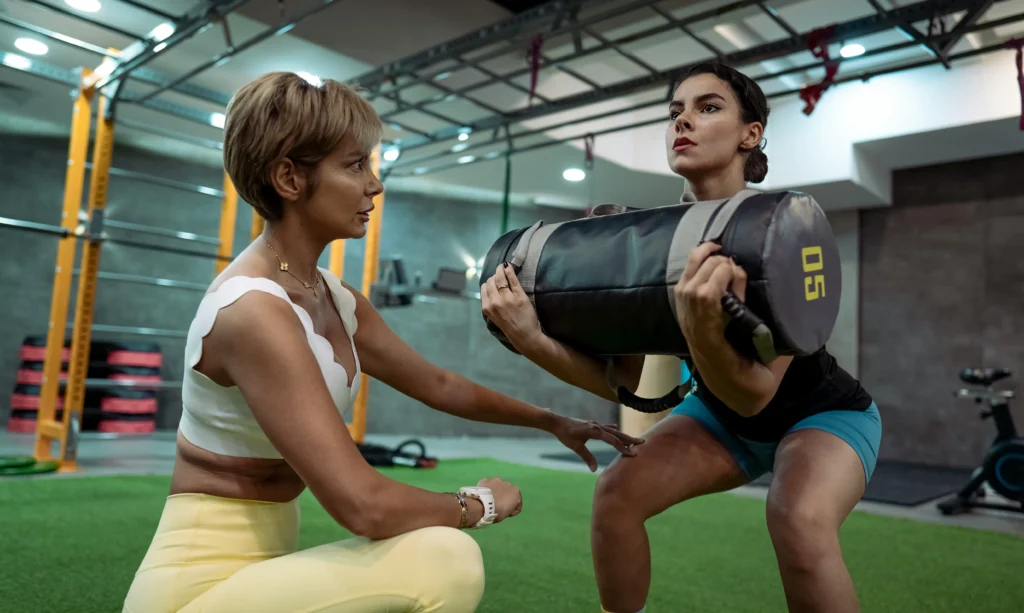 Photo of a woman doing squats under the guidance of a trainer at the gym