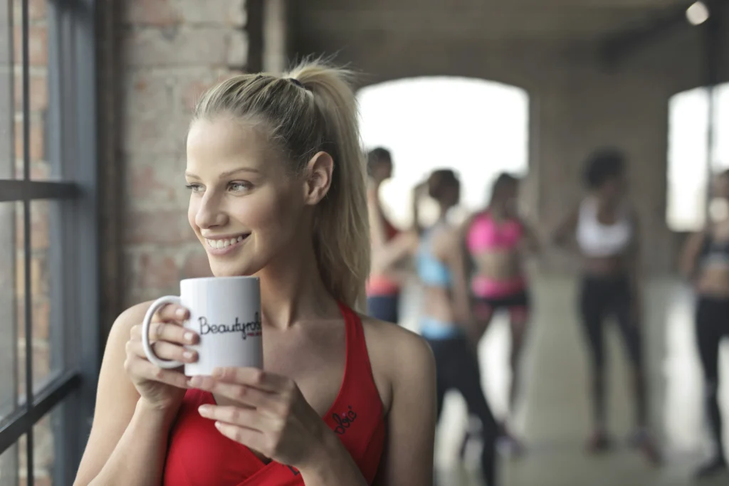 Smiling woman holding a white ceramic mug near a glass window at the gym