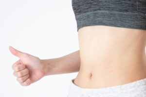 Woman giving a thumbs-up near her waist after dieting at a personal gym in Osaka