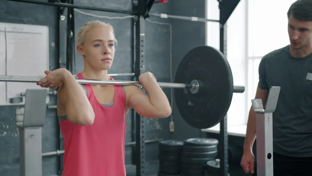 Woman lifting barbell under trainer supervision