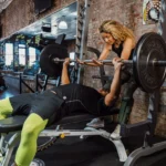 ジムでベンチプレスを持ち上げる男性と女性トレーナー