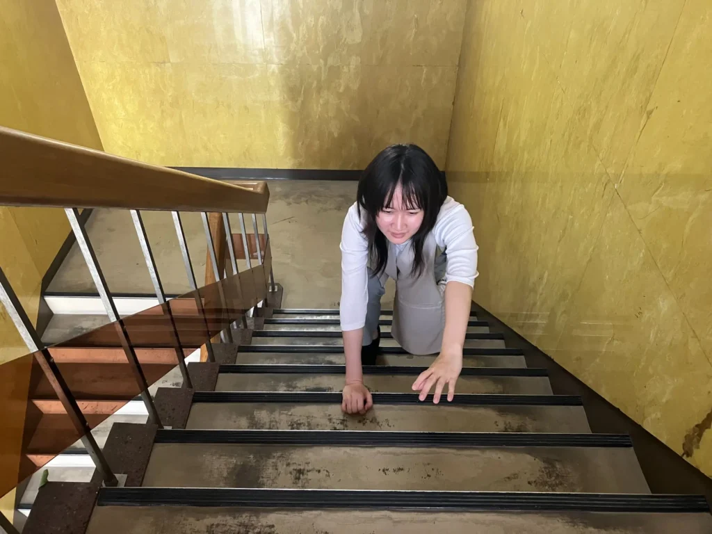 トレーニング後の筋肉痛のため、階段を上るのに苦労しているデザイナーNさん