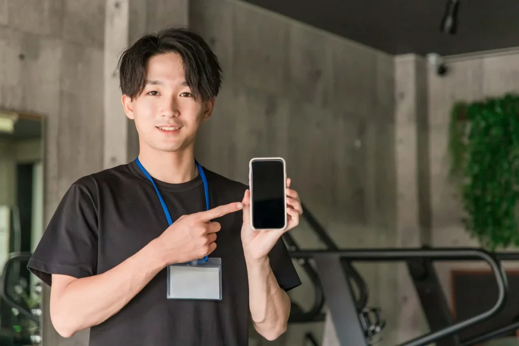 A male trainer in the gym holding a smartphone and pointing