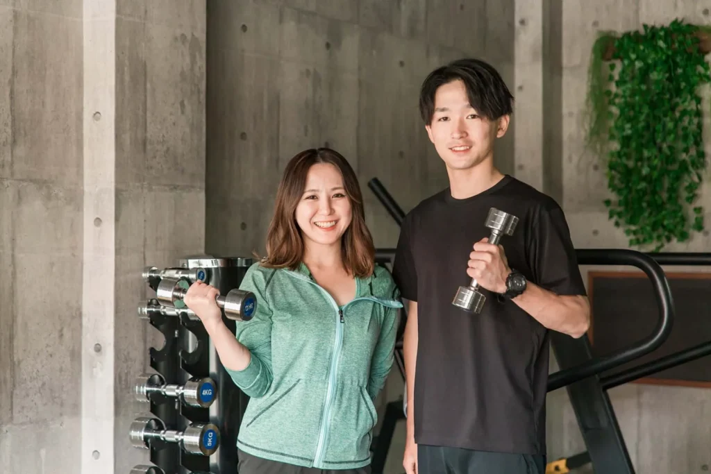 A man and woman smiling in the gym holding a dumbbell