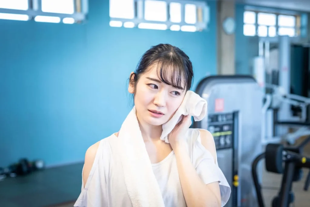 A woman in the gym wiping sweat with a towel while thinking